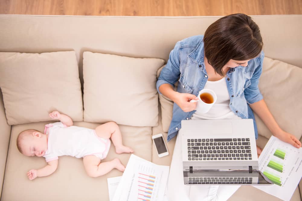 Mama werkt terwijl baby in zetel slaapt. Loopbaanexpert geeft tips voor thuiswerken met kinderen.