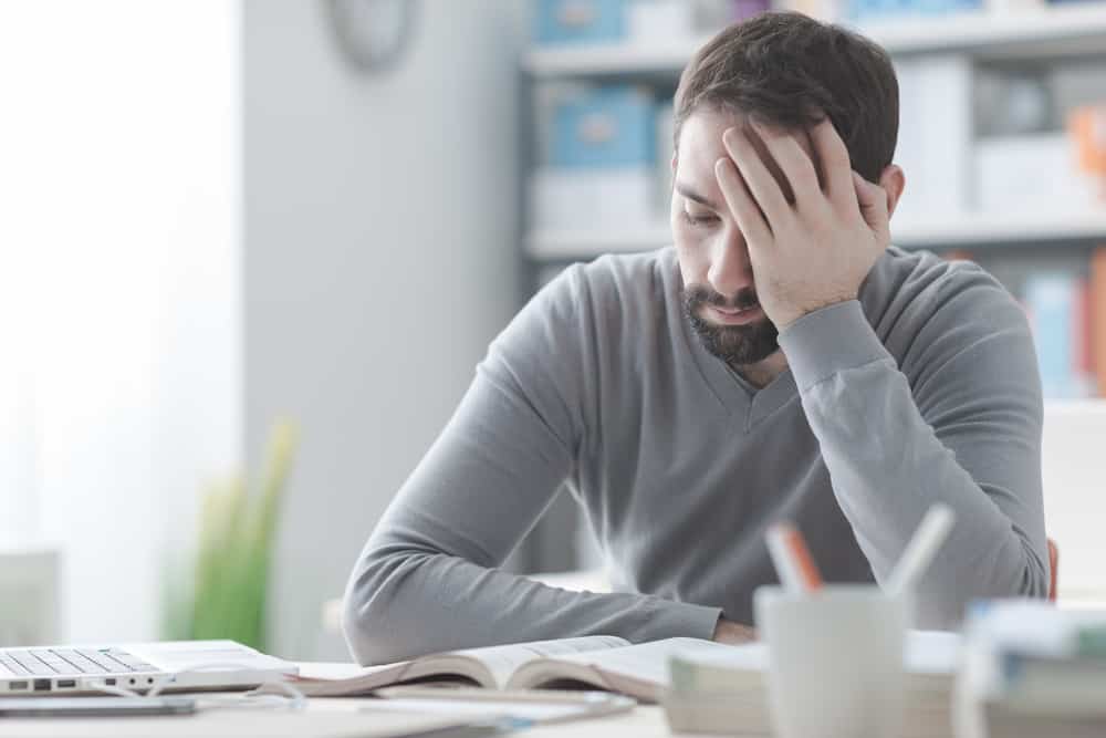 Verveelde man zit aan bureau en kan loopbaanbegeleiding gebruiken - Loopbaanexpert